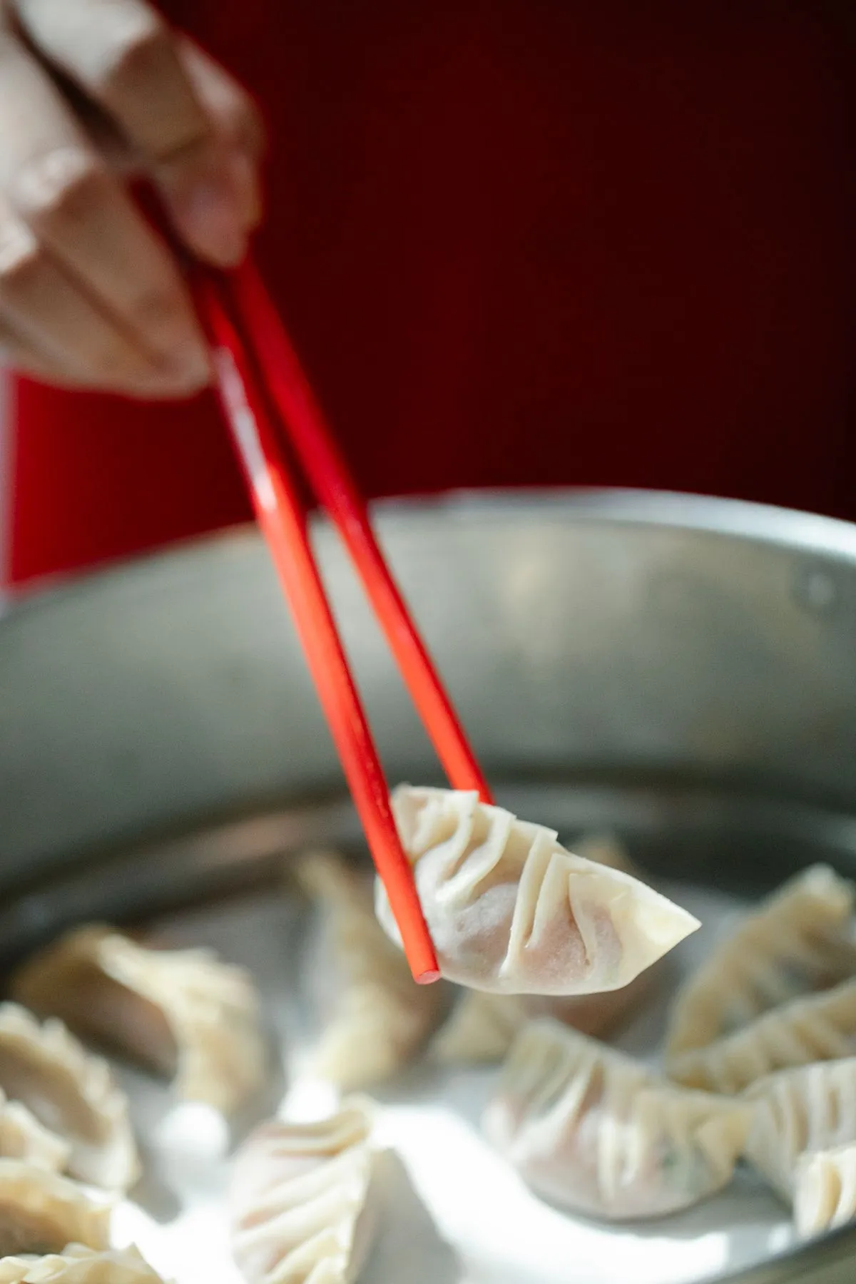Hand picking a jiaozi dumpling with red chopsticks from a steamer