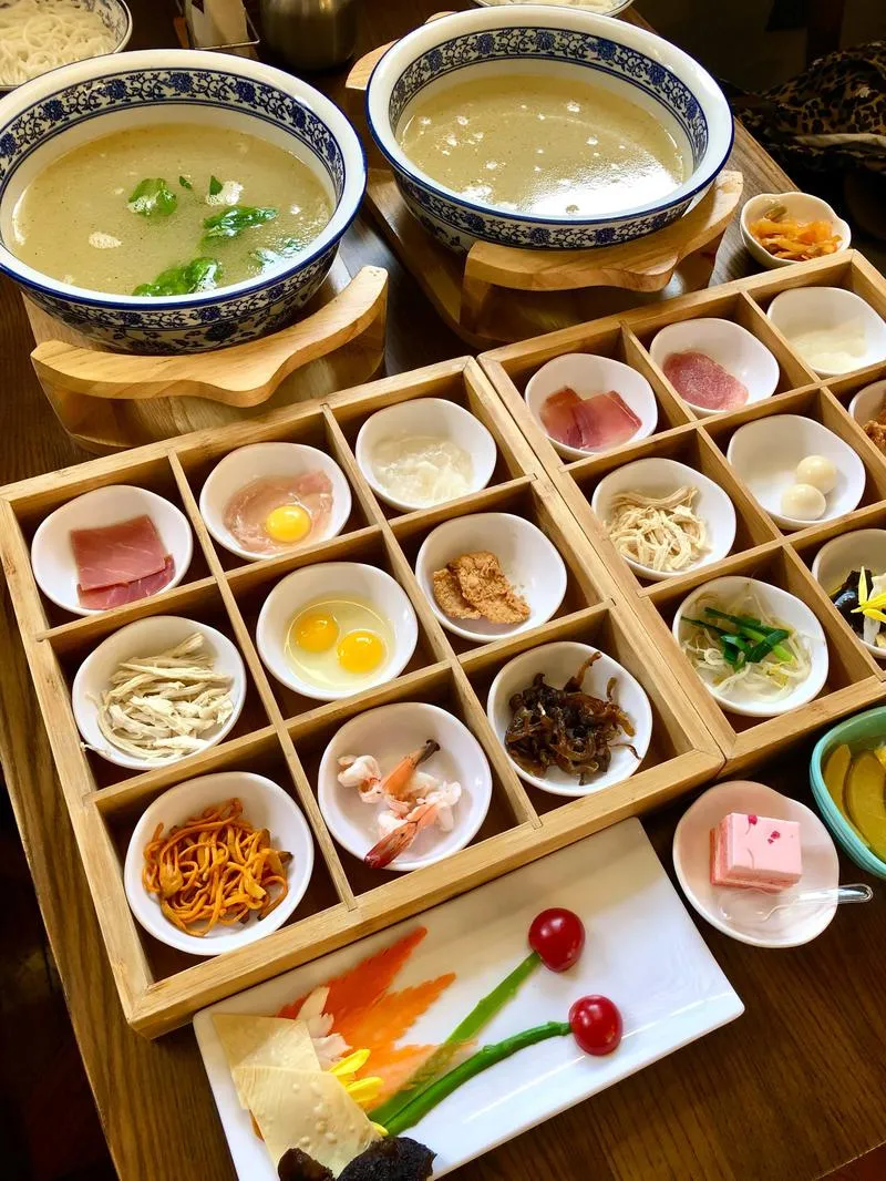 Crossing-the-Bridge Noodles — a bowl of boiling chicken broth with dozens of ingredients arranged for sequential addition